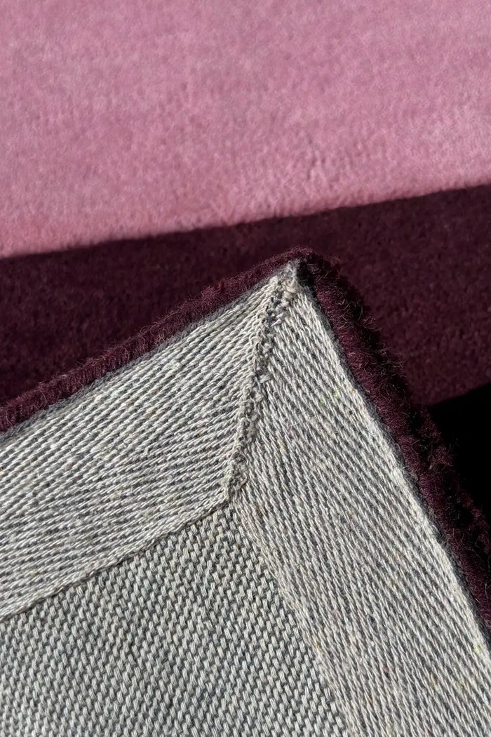 Blush and plum pink rug corner flipped to show stitched edge and backing, handmade wool rug for living room berry
