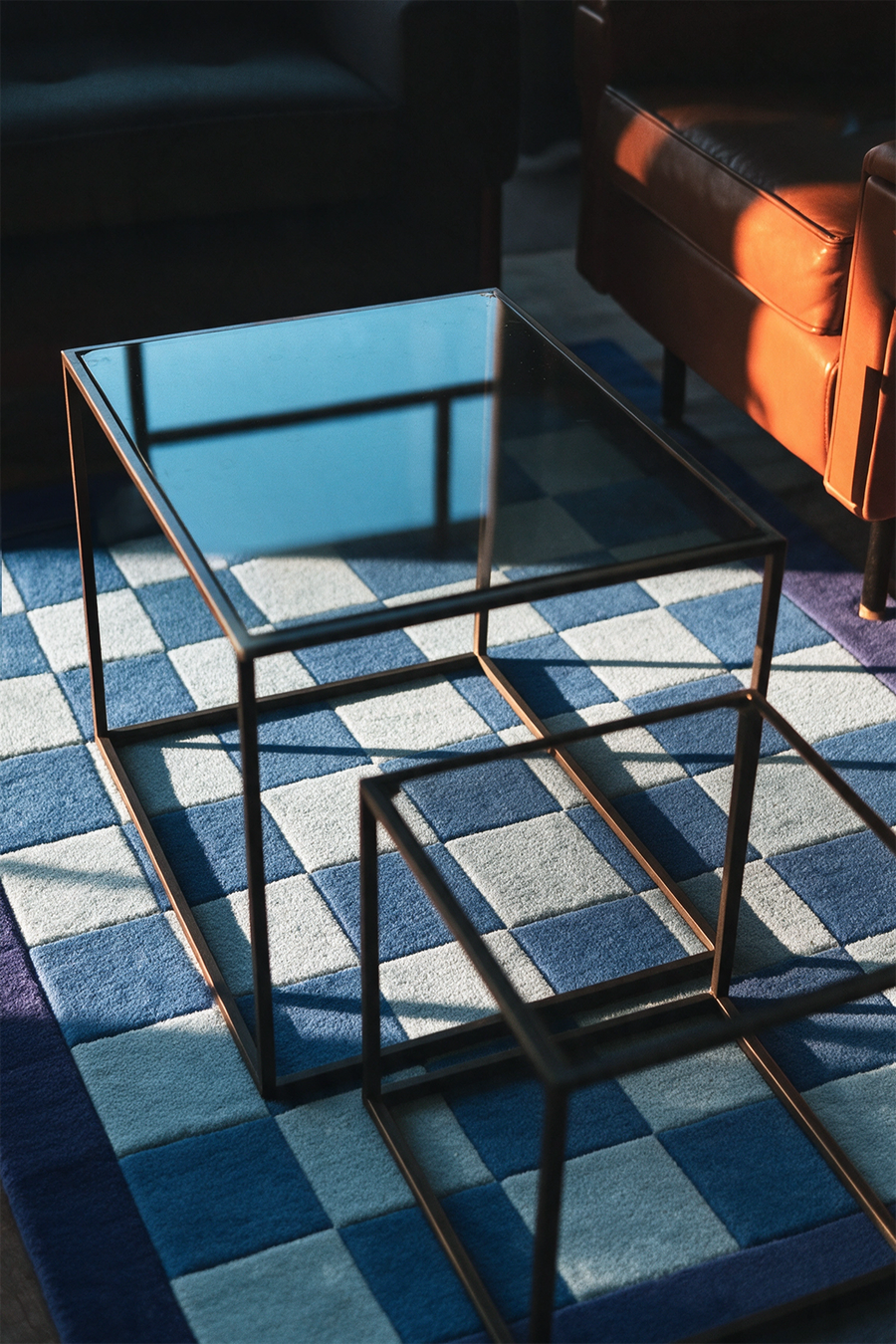 a blue checkered wool rug under a glass-top coffee table and leather sofa in a living room lifestyle