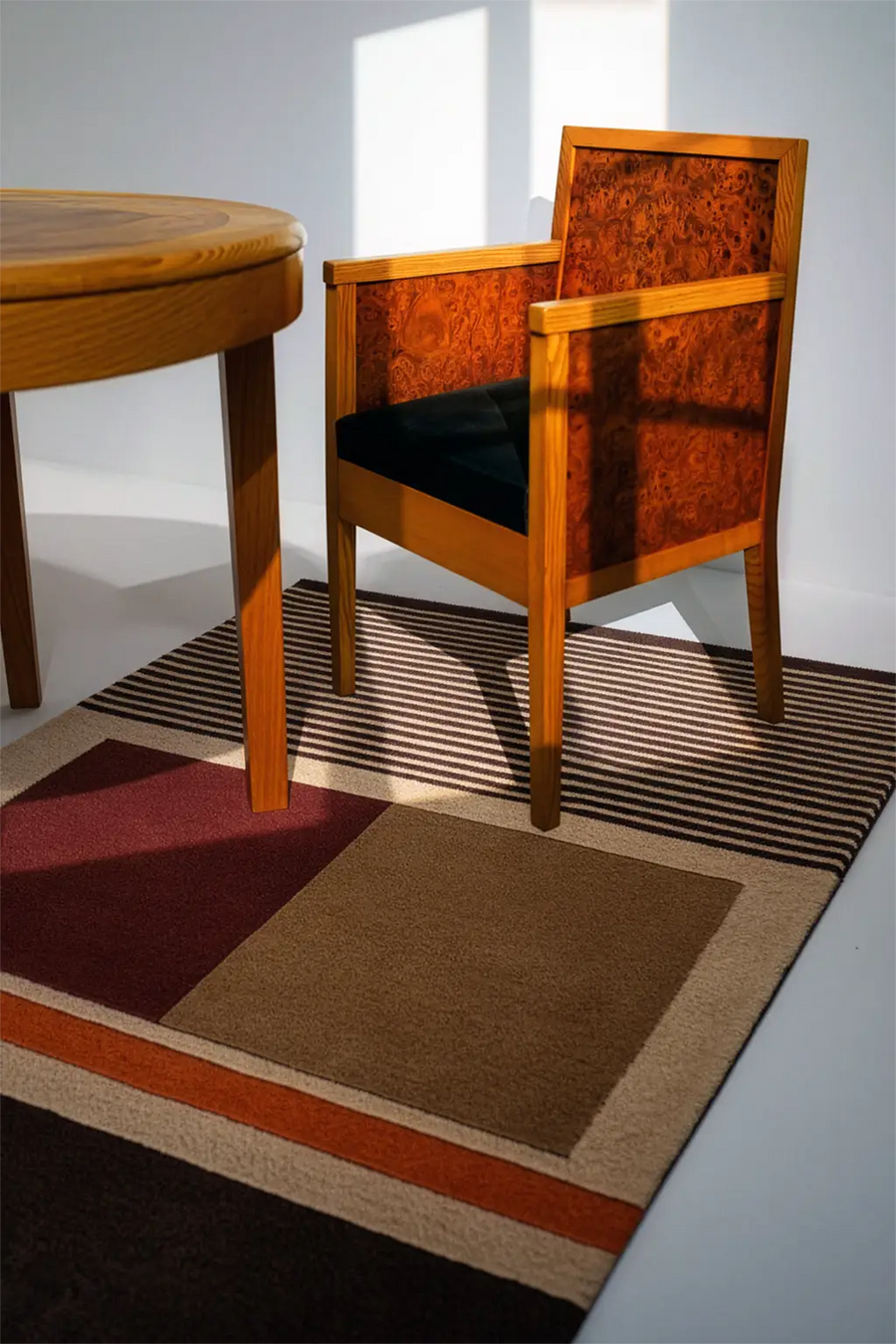 Wooden chair with black cushion on a earth toned patterned rug in a room with a round wooden table lifestyle