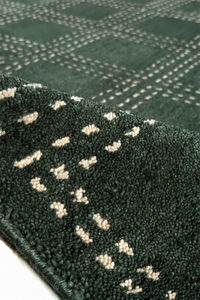 Close-up of a dark green textured square rug with a repeating geometric pattern of small light beige shapes.