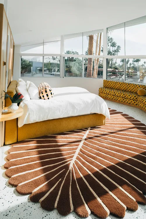 Modern bedroom with a large round brown floral leaf shaped rug, bed, and large windows.