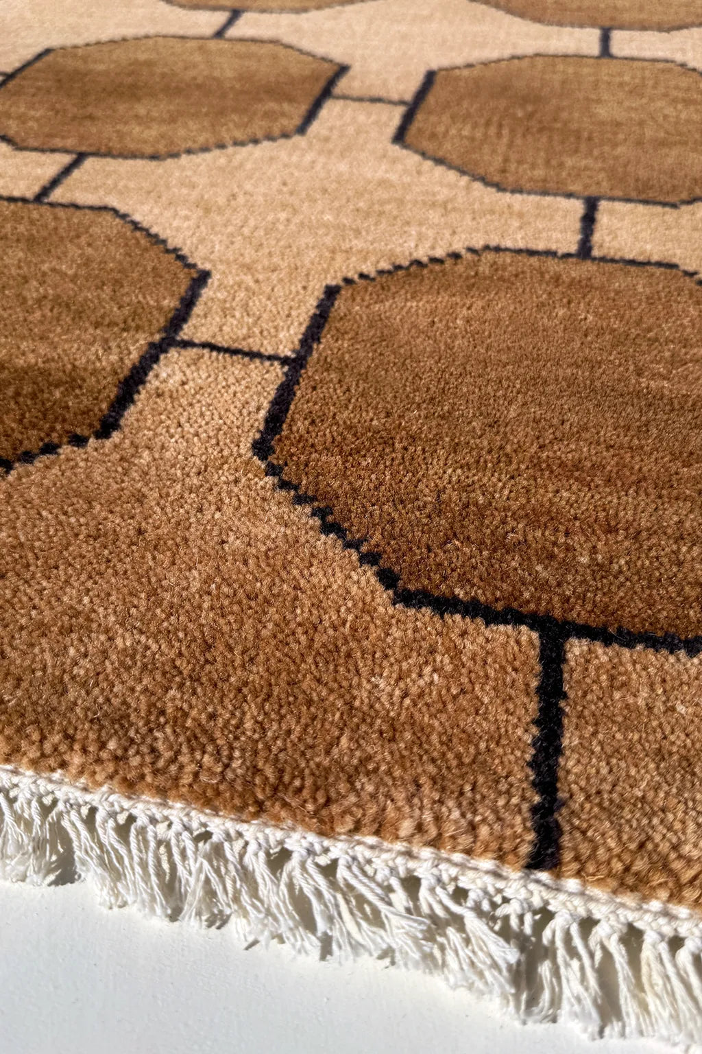 golden brown geometric patterned rug with a white border on a neutral background