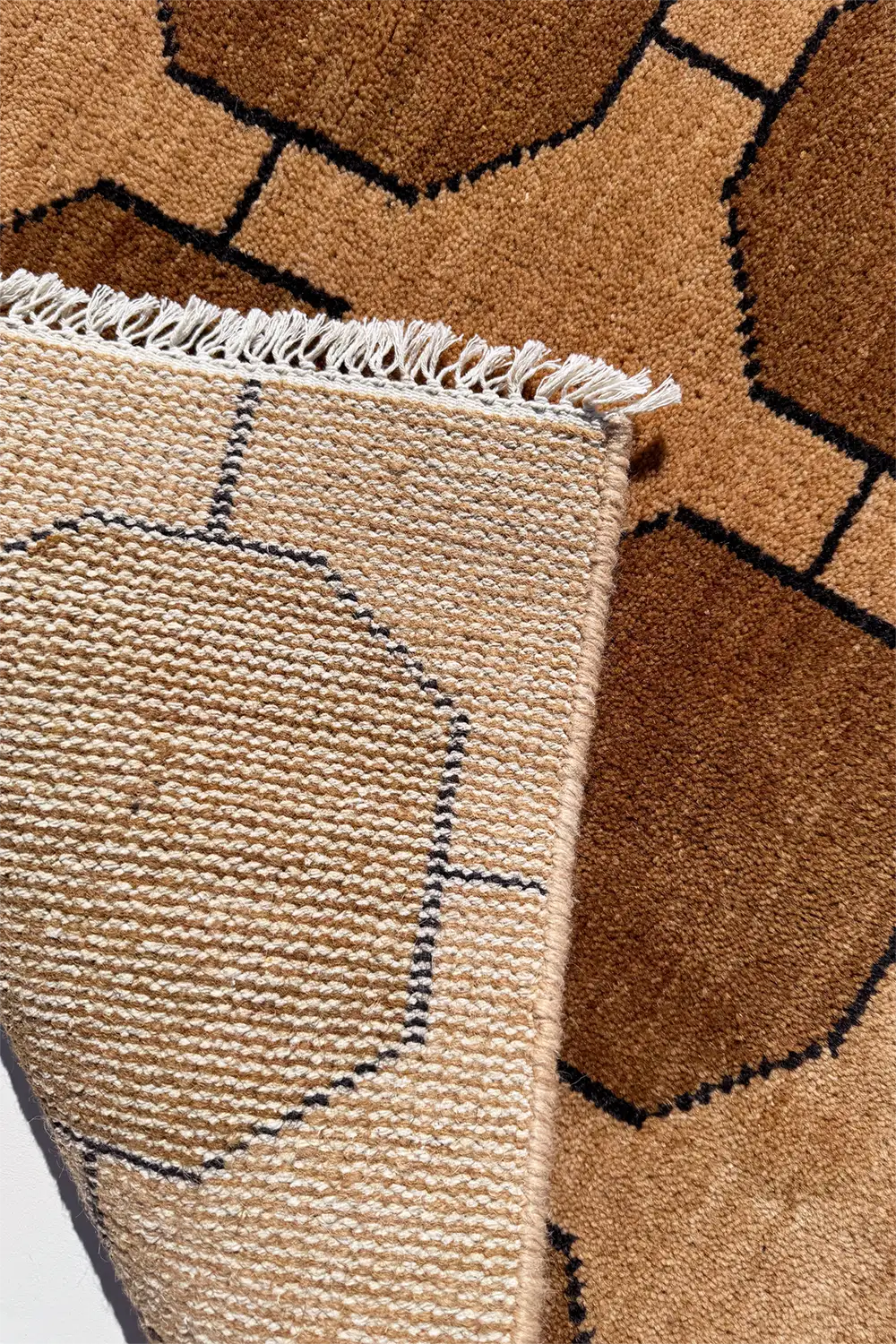 Close-up of a textured warm neutral brown and beige rug with geometric pattern and fringe