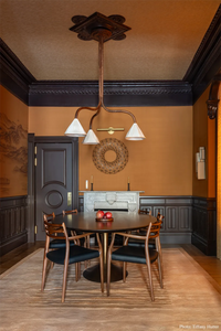 Dining room with elegant gold rug, wooden table and chairs, chandelier, and decorative wall mirror.