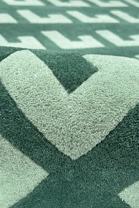 Close-up of a textured green square rug with geometric pattern