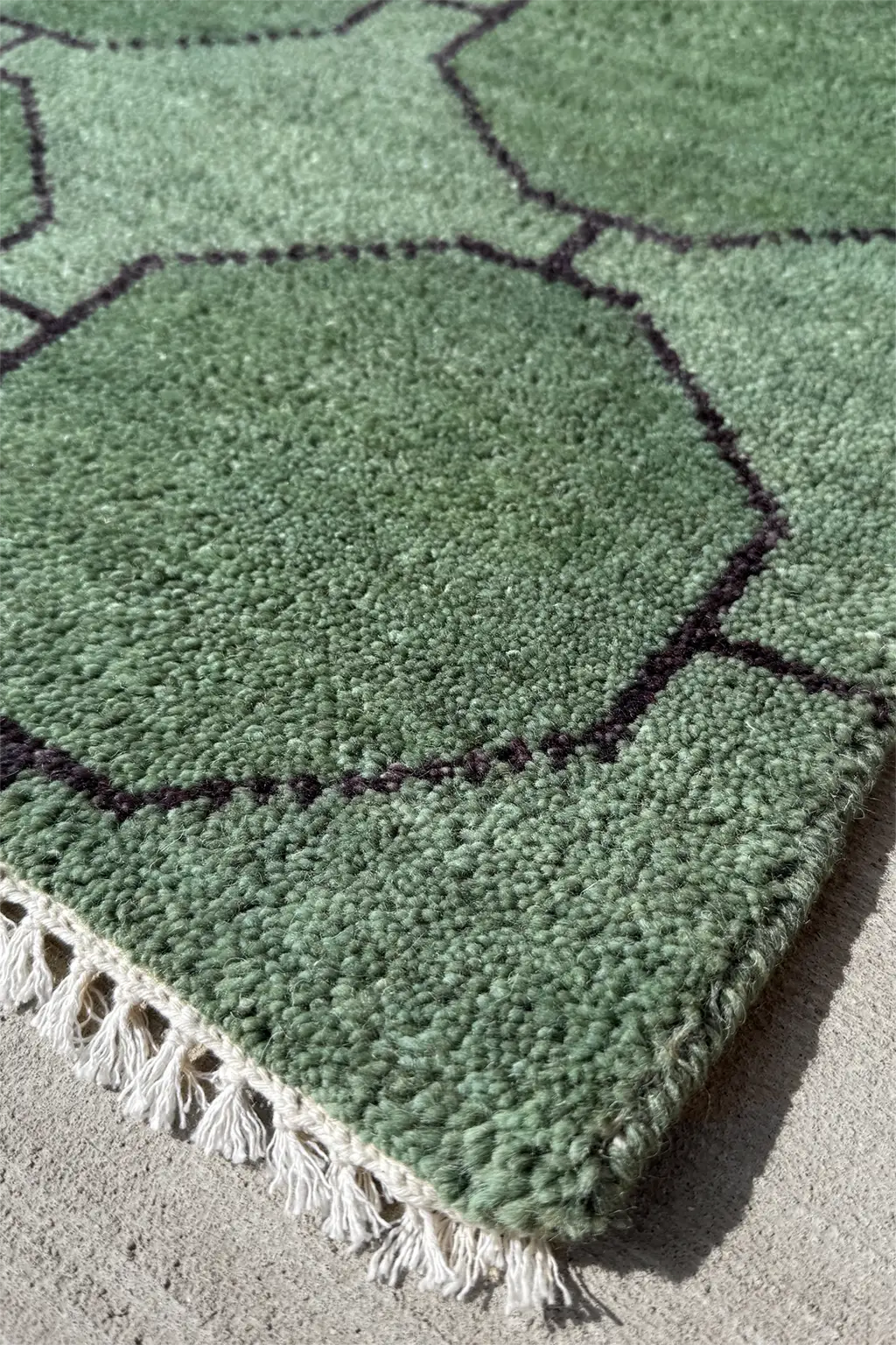Green geometric patterned rug with white tassels on a concrete floor texture