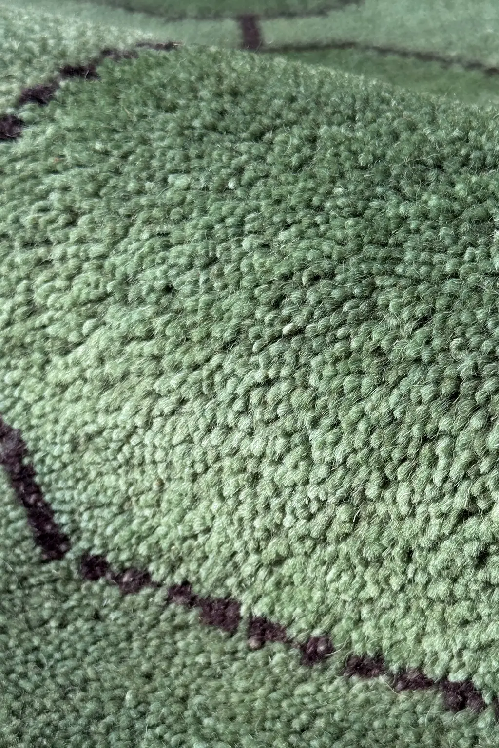 Close-up of a textured green knotted geometric rug with black accents texture