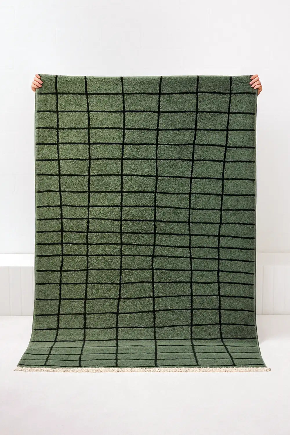 Green grid knotted area rug held up against a white background