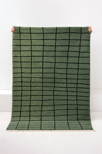 Green grid knotted area rug held up against a white background lifestyle