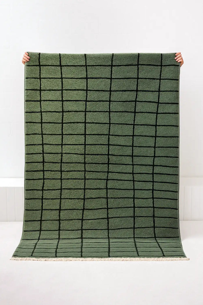 Green grid knotted area rug held up against a white background lifestyle