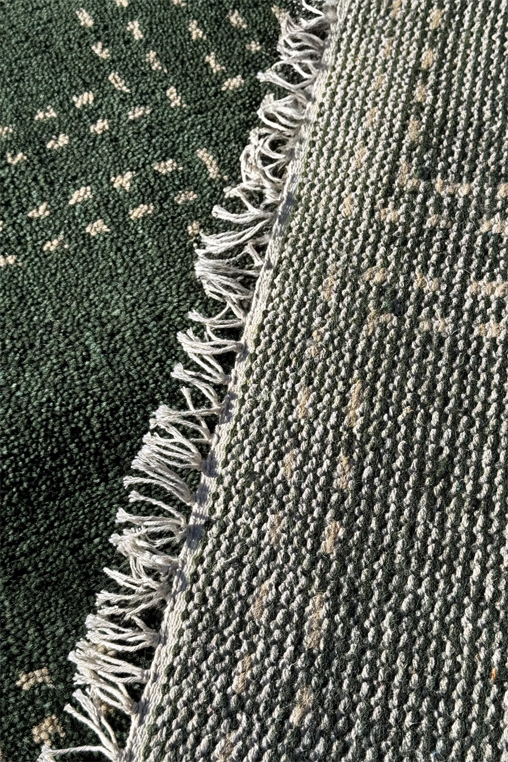 Close-up of knotted runner rugs with fringe, one dark green with small cream motifs and one gray-green with a subtle beige pattern.