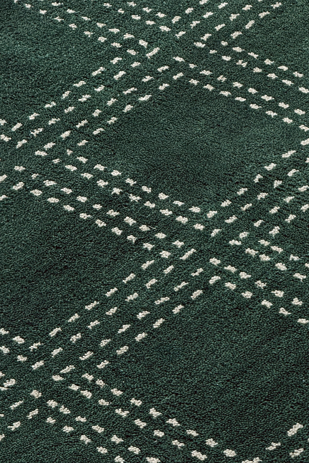 A close-up of a dark green textured rug with a repeating white dotted geometric diamond pattern.