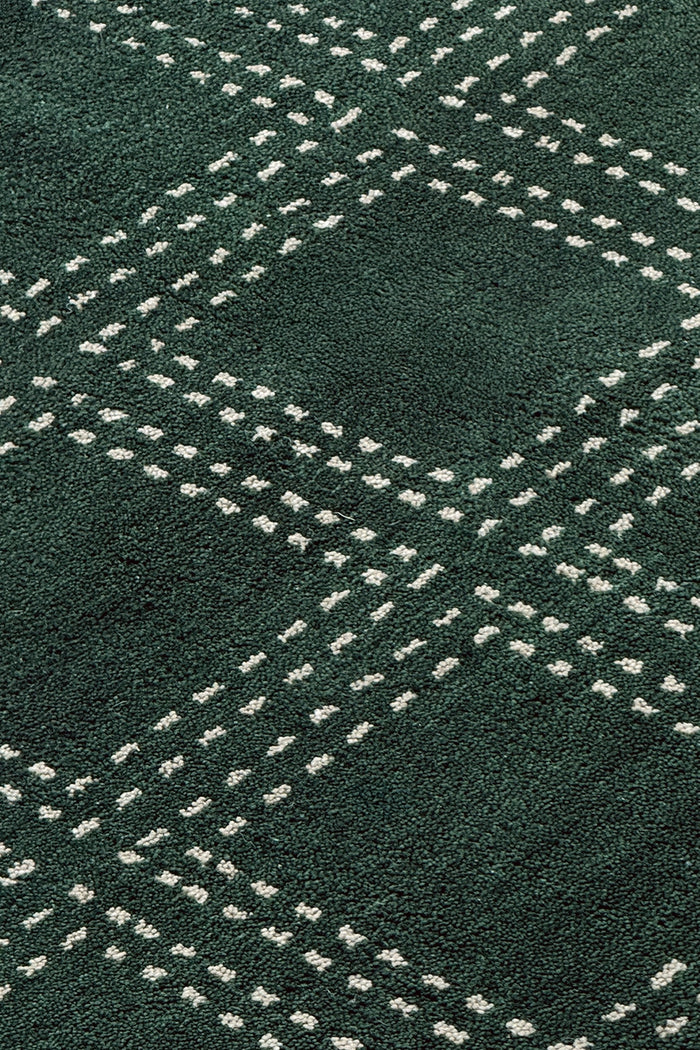 A close-up of a dark green textured rug with a repeating white dotted geometric diamond pattern.
