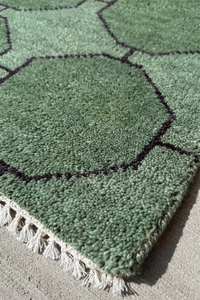 Green runner rug with geometric pattern and white tassels on a concrete floor