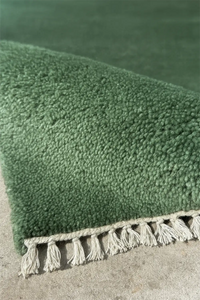 Green knotted wool rug with tassels on a textured surface