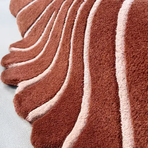 Close-up of a rust-colored tufted rug with scalloped edges and white carved lines showing plush texture