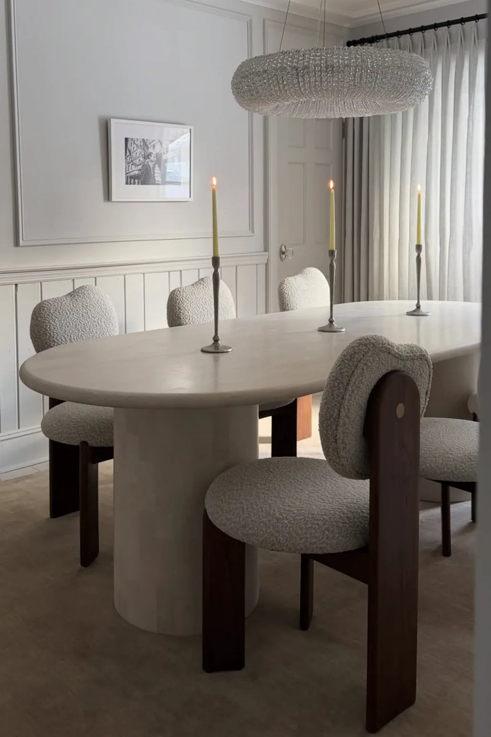 Dining room with a round table and chairs on a neutral rug, featuring a chandelier and framed picture on the wall.