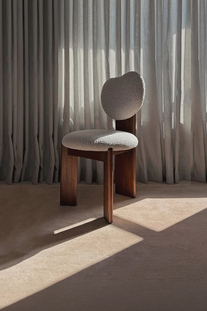 Modern chair with wooden frame and upholstered seat and back against a curtain backdrop on a stone rug