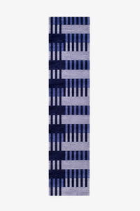 A long, narrow runner rug with a geometric pattern of vertical stripes in navy, medium blue, and light lavender-gray on a white background.