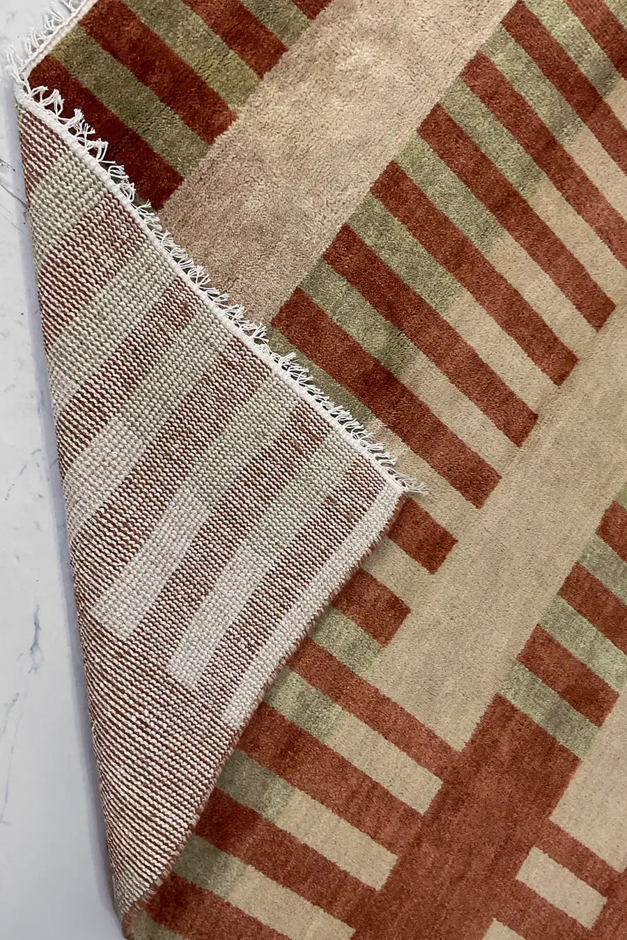 striped hand knotted wool rug with geometric bands of burnt orange, tan, and olive green