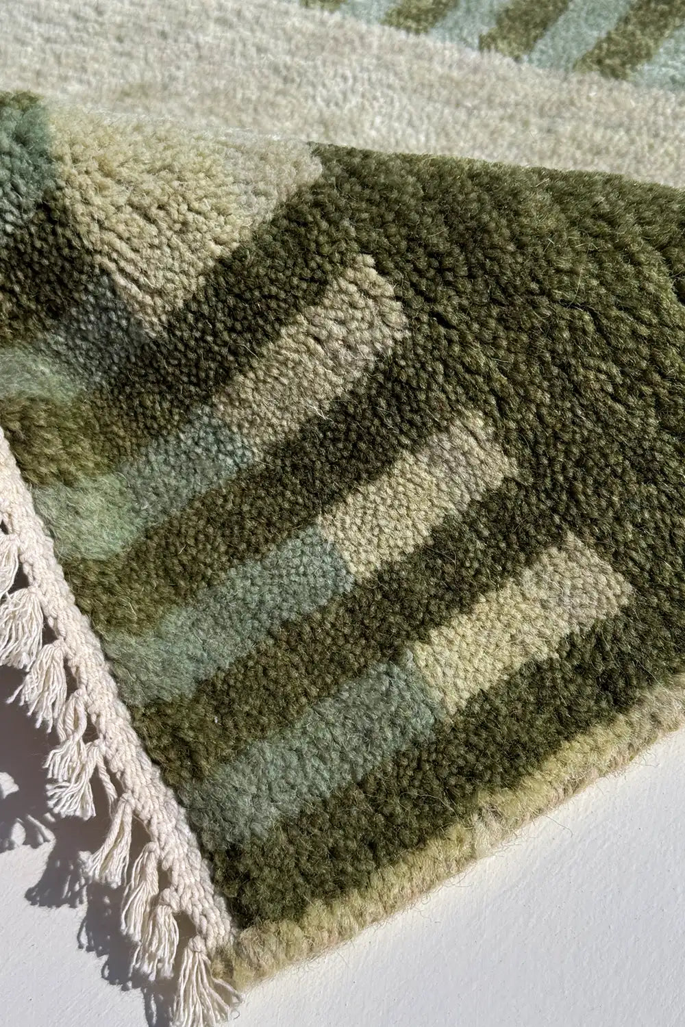 Close-up of a green and olive striped rug with tassels on a white background