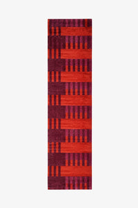 A long runner rug with a geometric pattern of alternating horizontal bands in bright red-orange and deep magenta-purple, featuring vertical stripe motifs.