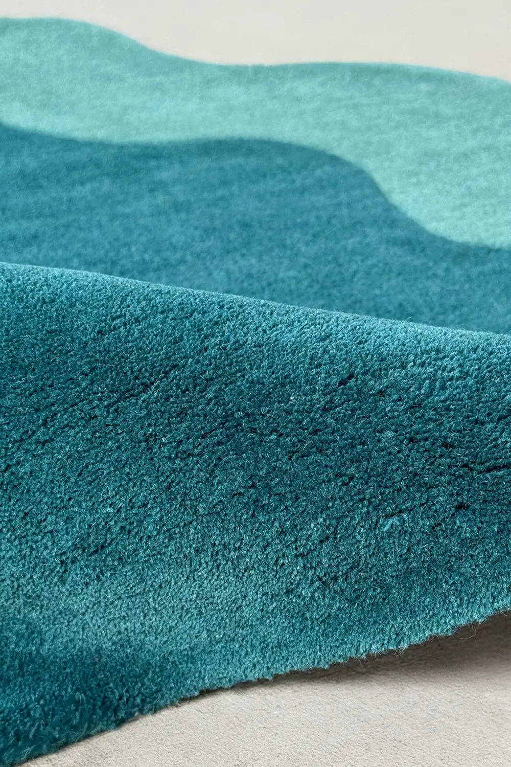 Close-up of deep teal wool pile in corner circle rug with a wavy abstract edge, perfect for modern living rooms or colorful entryways
