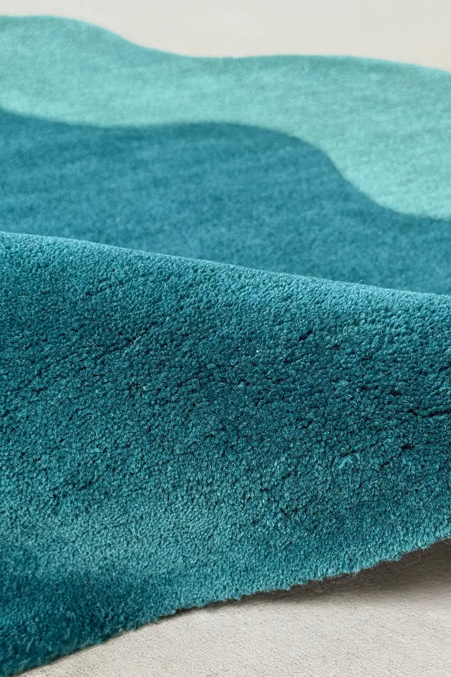 Close-up of deep teal wool pile in corner circle rug with a wavy abstract edge, perfect for modern living rooms or colorful entryways