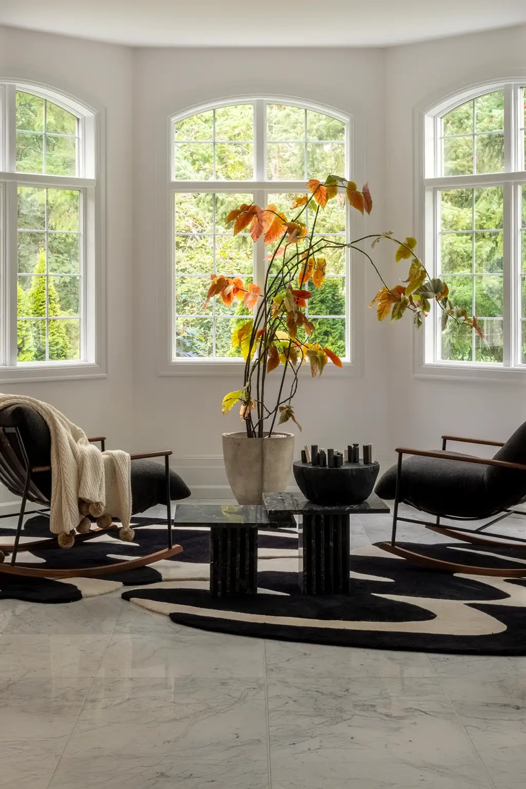 Modern living room with large windows, black chairs, unique black and white zig zag rugs, and a central chess table with a vase of flowers lifestyle