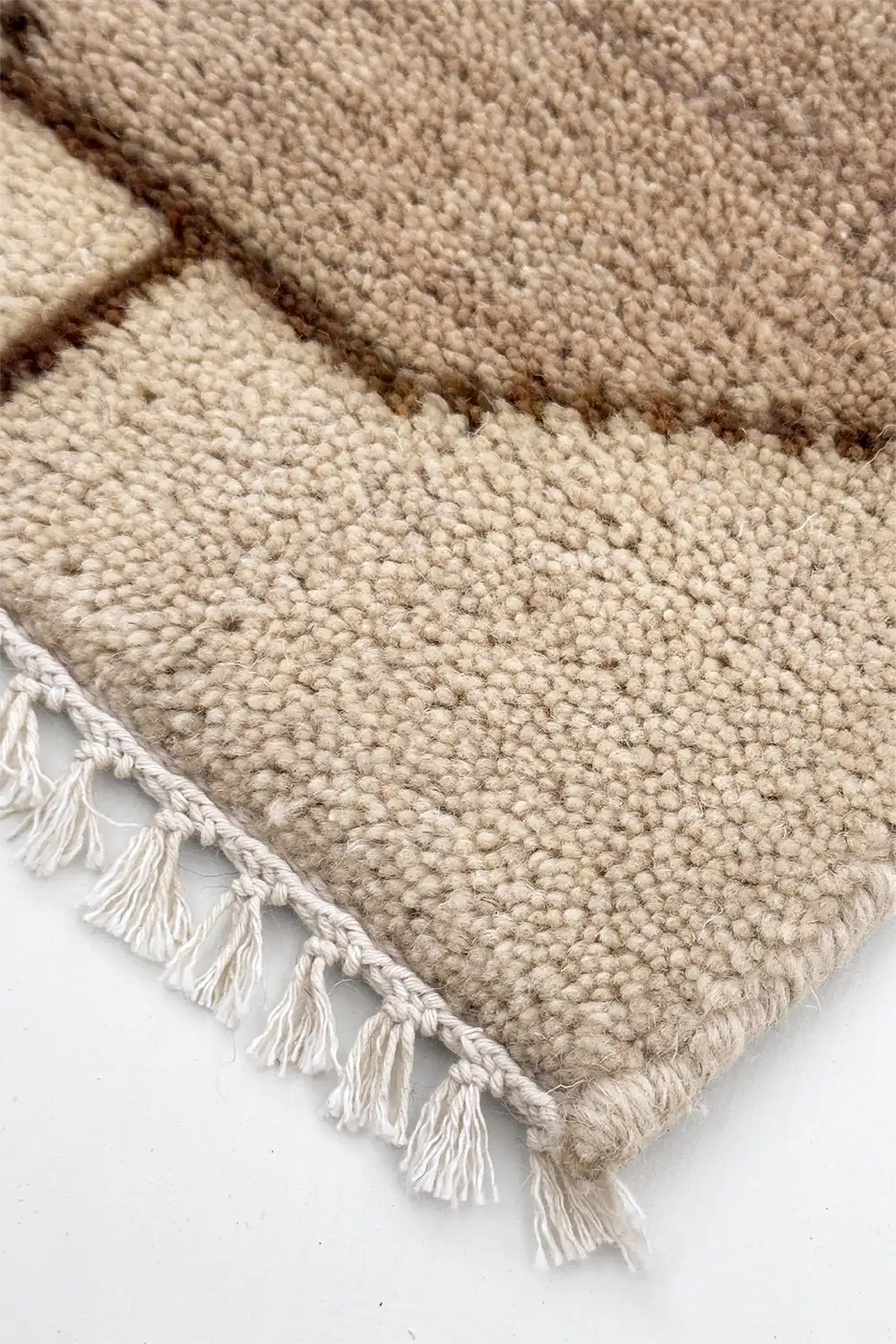 Close-up of an off white textured area rug with geometric pattern and tassels on a white background