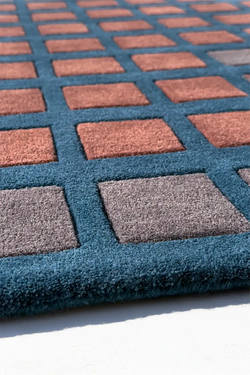Close-up of a textured rug with a checkered pattern in brown rust teal blue and gray on a white background