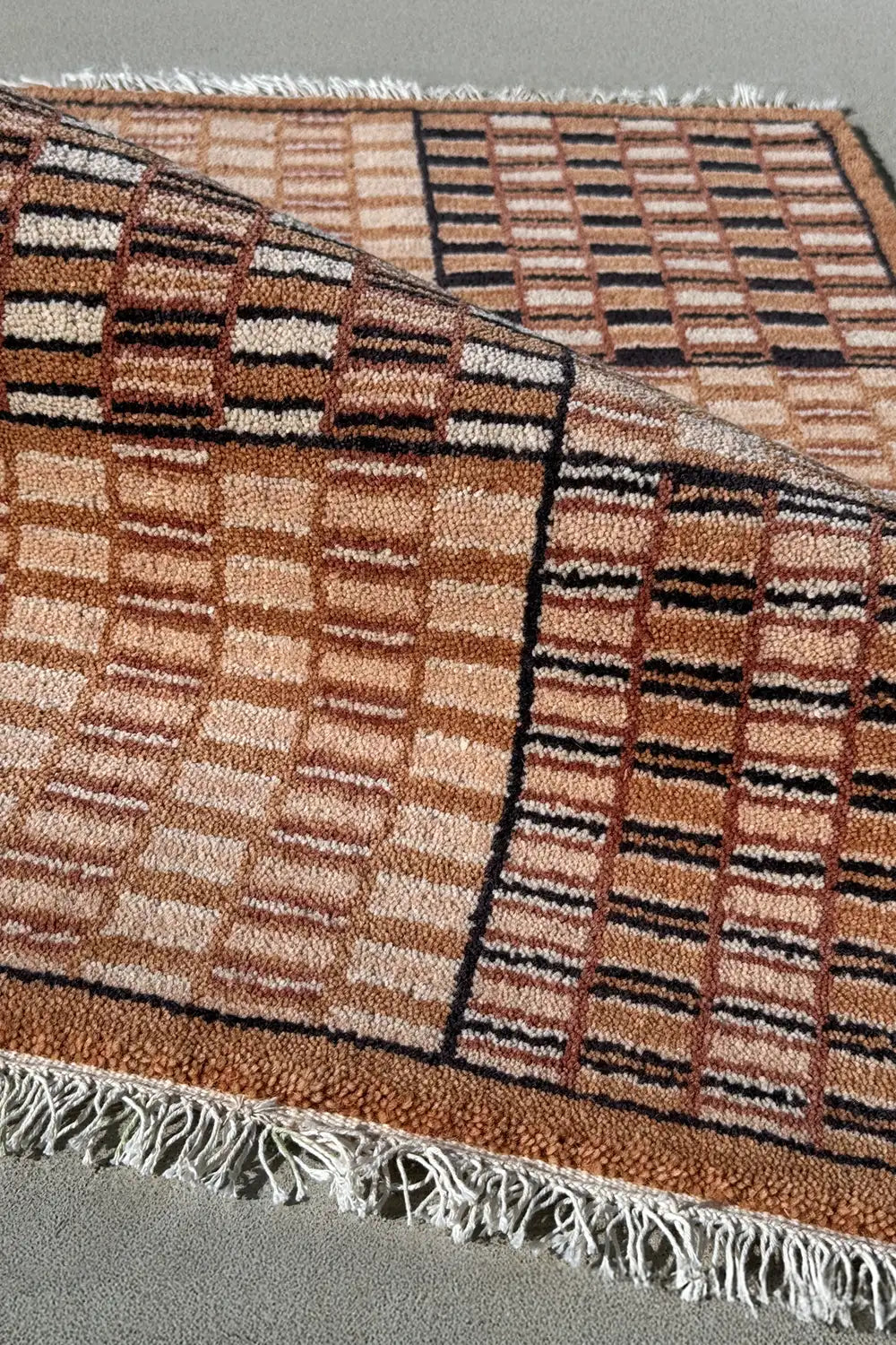 Close-up of brown and cream wool rug with bold checkered print, woven mid-century modern texture in warm tones