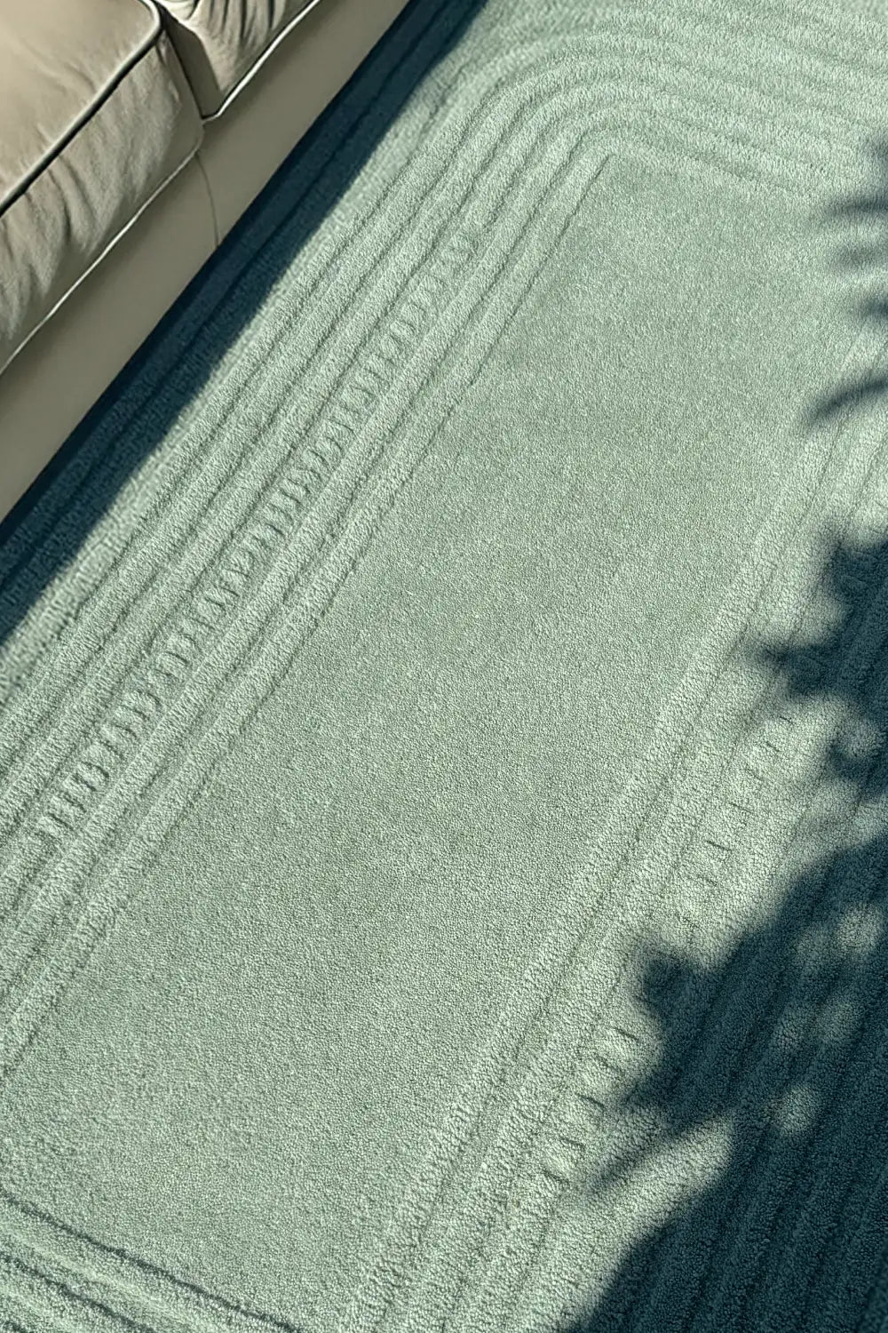 Close-up of a textured light green modern rug with a neutral-colored sofa in the corner.
