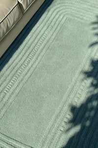 Close-up of a textured light green modern rug with a neutral-colored sofa in the corner.