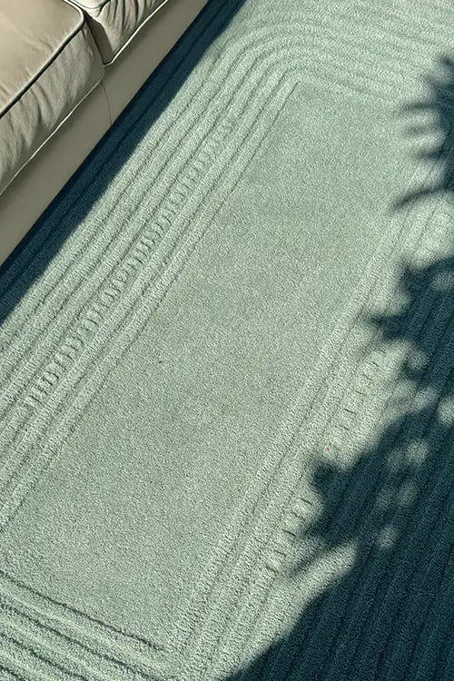 Close-up of a textured green rug with geometric pattern in a sunny minimalist living room