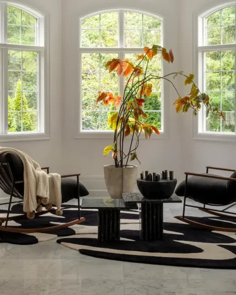 Modern living room with abstract rugs, black marble coffee table, chairs, and a large window.