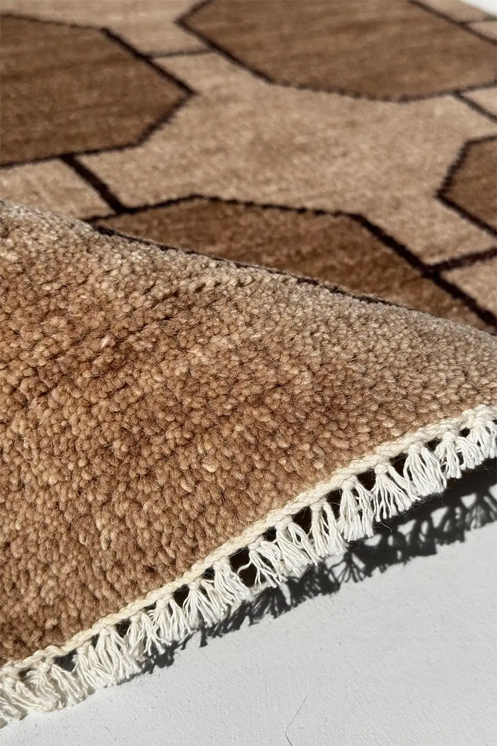 Close-up of a brown geometric patterned rug with white fringe on a light gray floor.