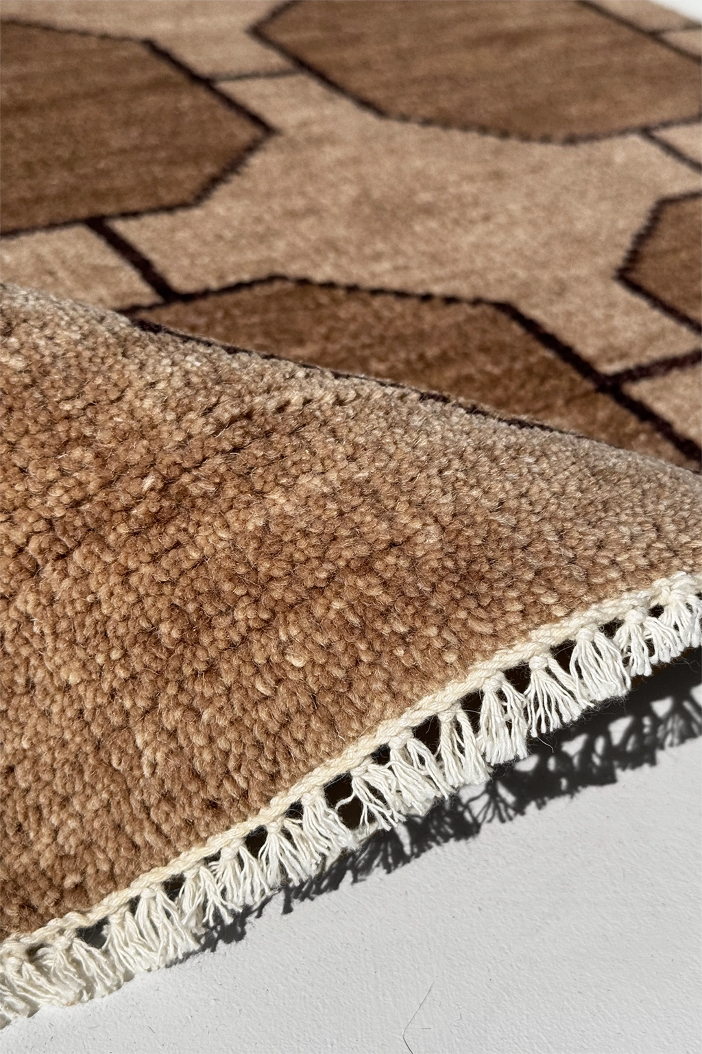 Close-up of a light brown geometric patterned rug with white fringe on a light gray floor.
