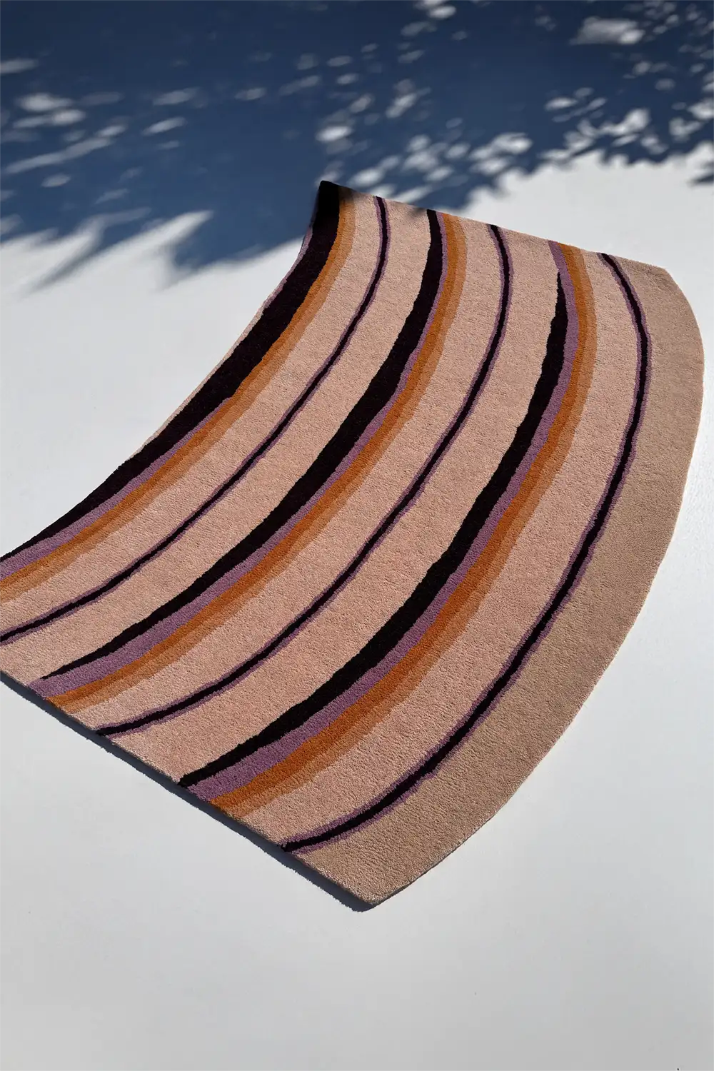 mid century striped rug with tan, purple, black, and orange pattern on a white surface lifestyle irregular shaped