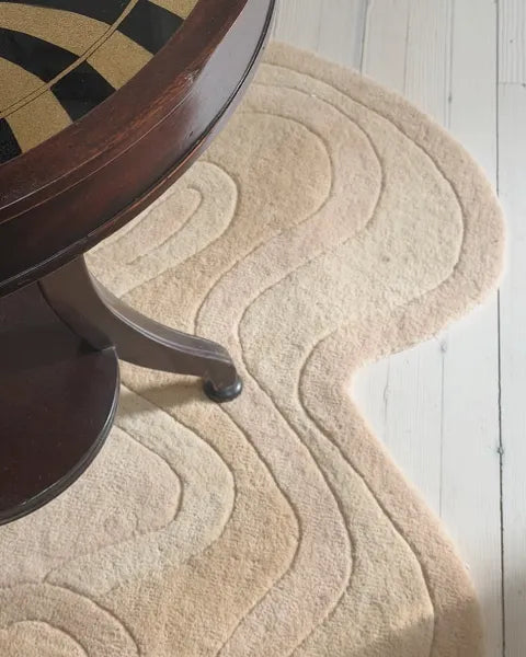 Beige textured rug on a light wooden floor with a dark wooden chair leg visible.