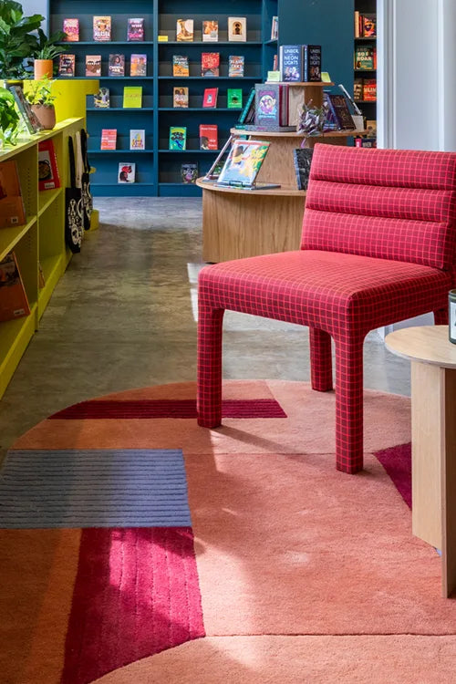 Red checkered chair in a colorful store interior with bookshelves and a patterned oval wool rug in custom colors.