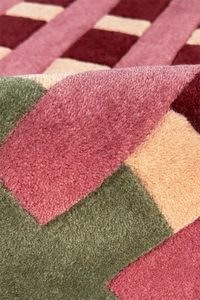 Close-up of a multicolored geometric patterned rug with shades of red, pink, green, and beige.