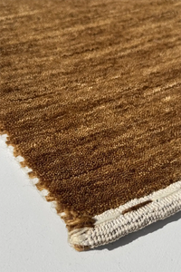 Close-up of a warm gold brown textured rug corner on a light gray background hazel