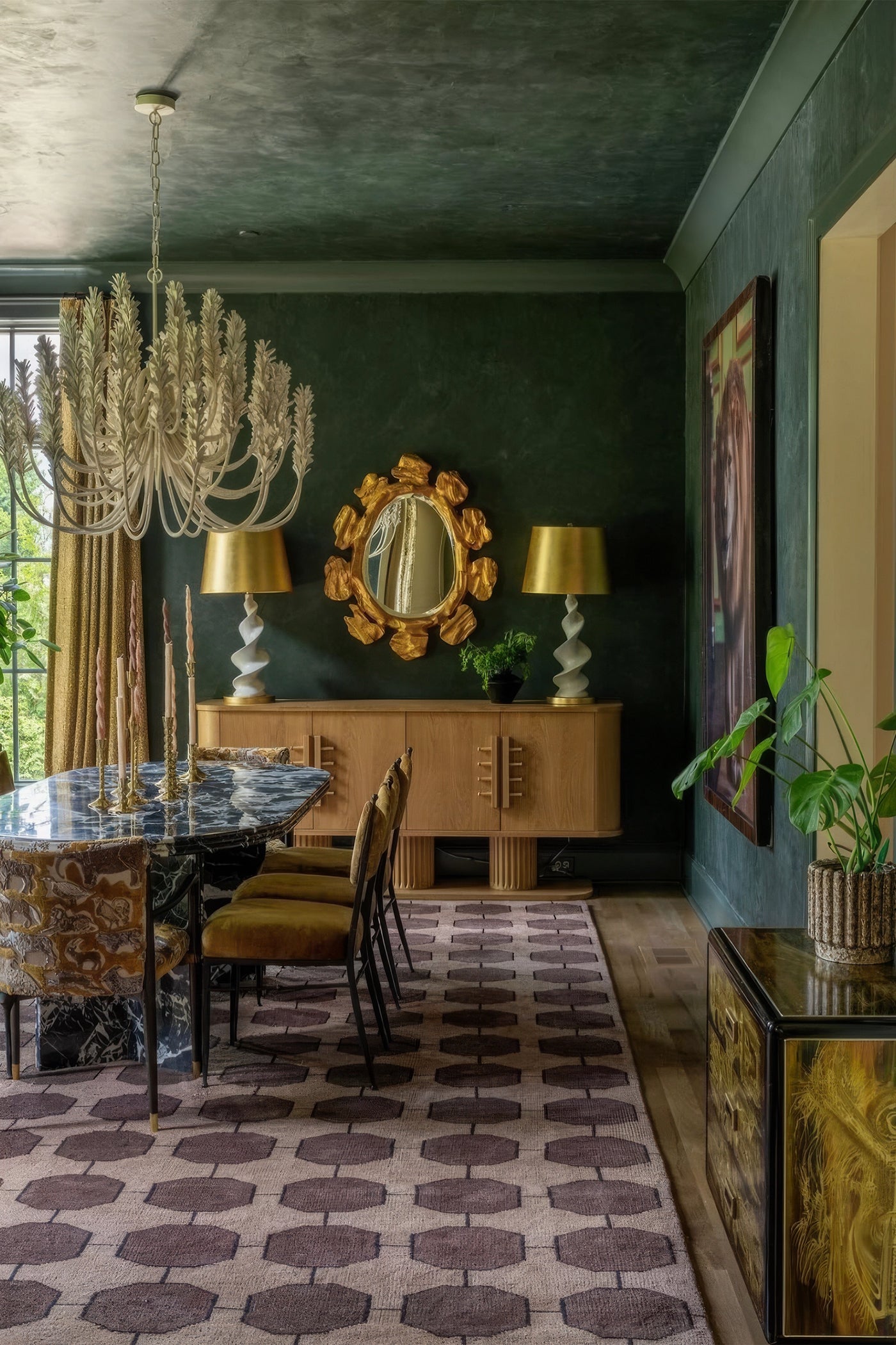 A styled dining room interior with a dark green wall, patterned walnut rug, chandelier, wooden console, gold lamps, and dining chairs. No person or animal is present, but this is a real interior environment rather than a clean isolated product shot, so subject_type is Lifestyle