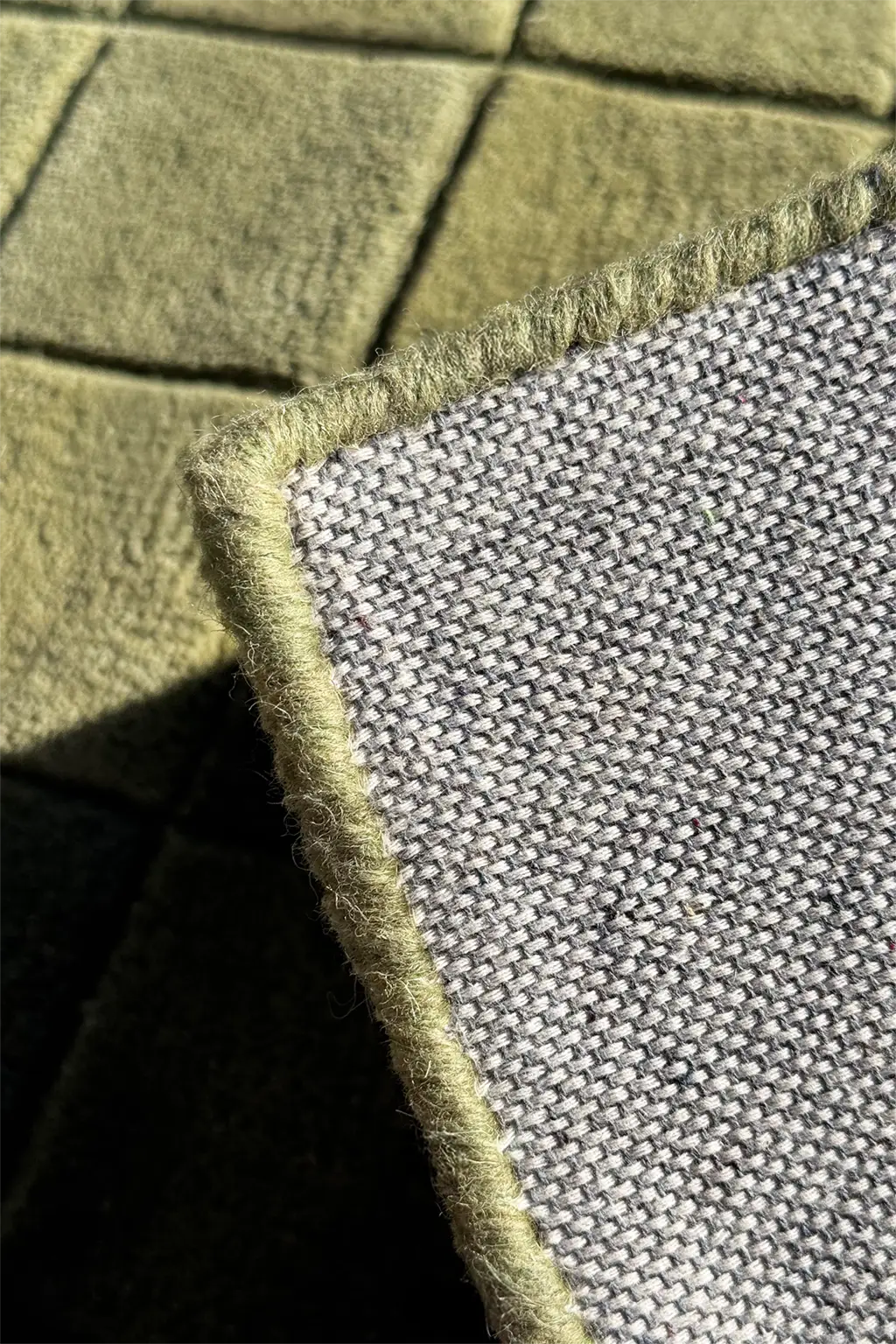 Close-up of a textured green checkered rug with serged edges