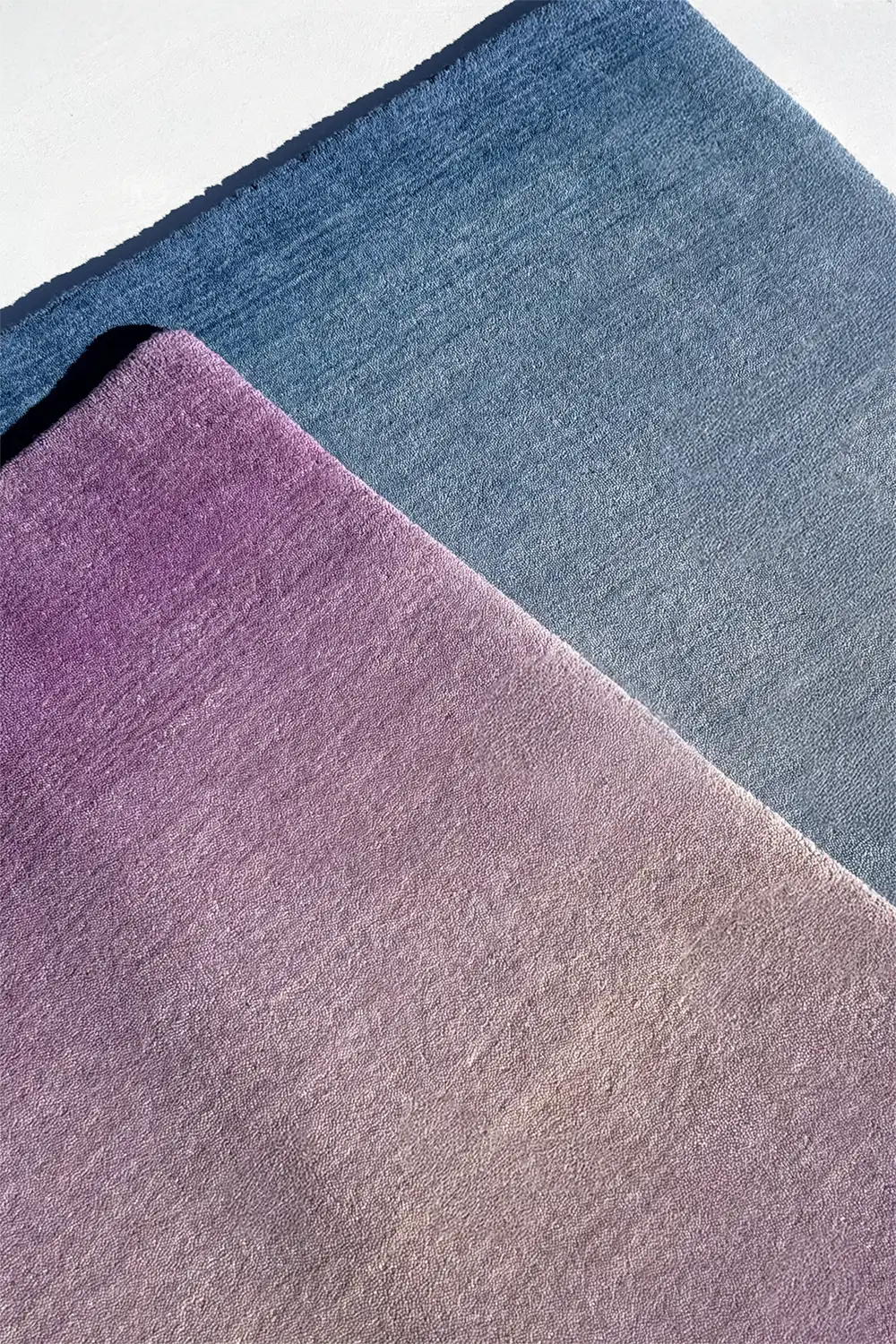 Two ombre loomed wool rugs, one purple and one blue, on a white background.