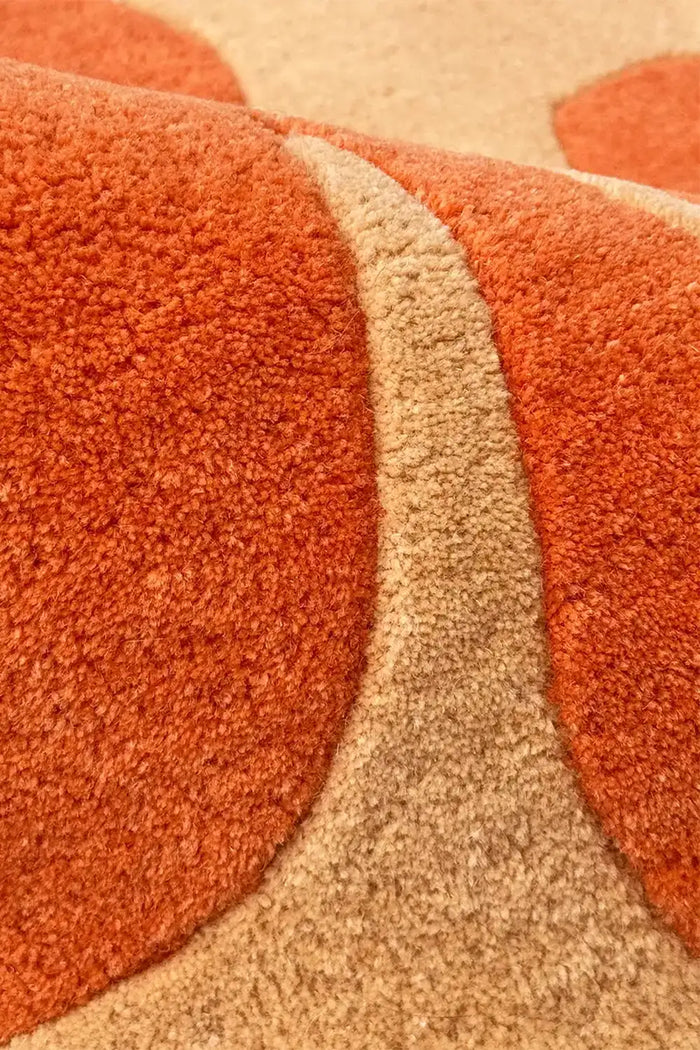 Close-up of a textured orange and beige wool rug with abstract floral patterns.
