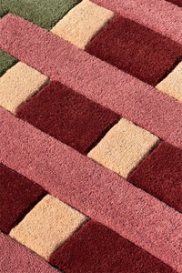 Close-up of a textured rug with geometric striped pattern in red, beige, and green.