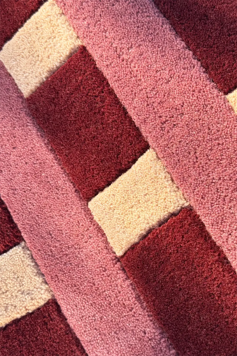 Close-up of a textured rug with geometric pattern in red pink and beige colors.