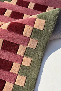 Close-up of a geometric patterned rug with red, green, and beige colors.
